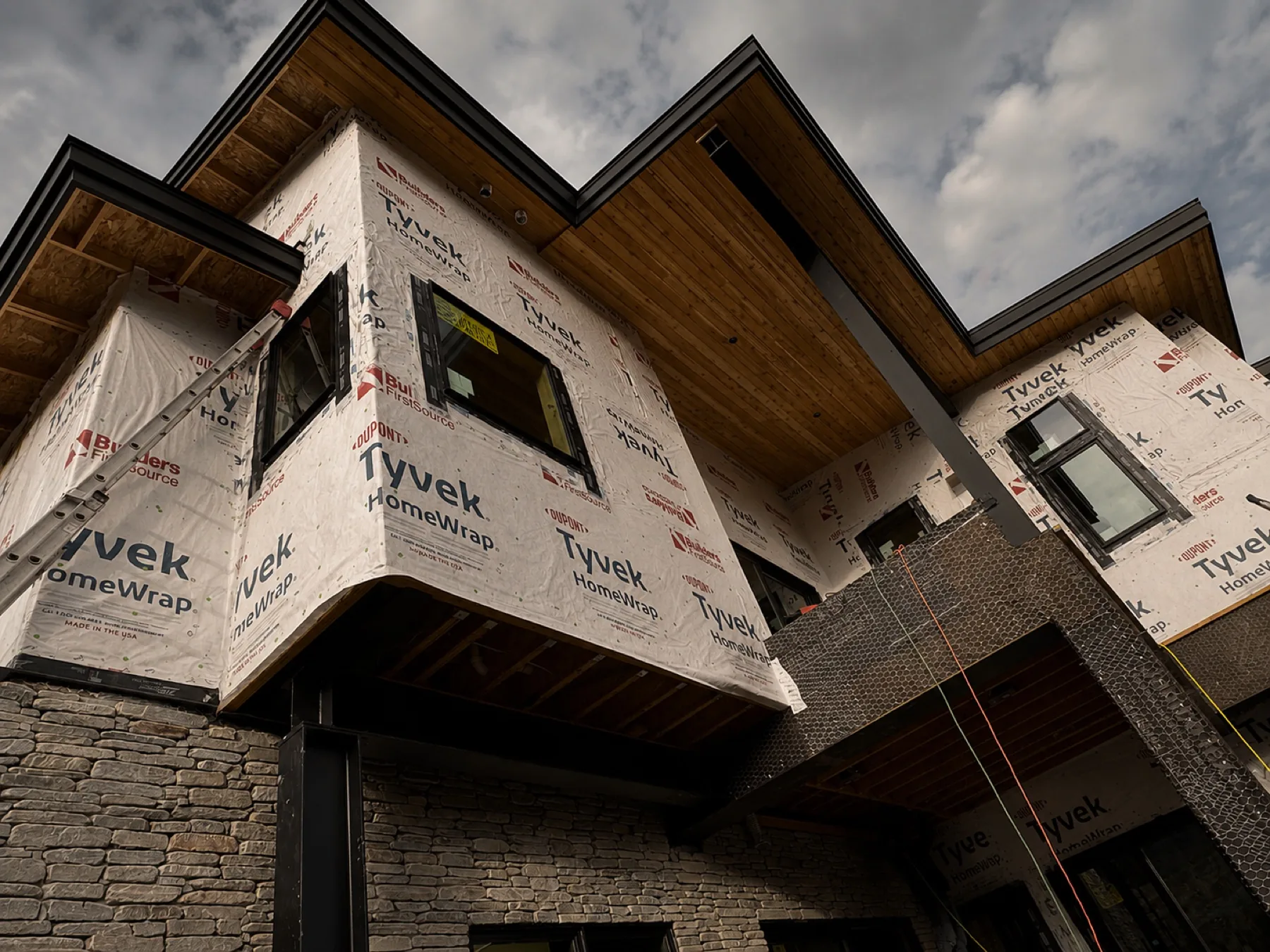 Upward angle of cedar soffit, black fascia and weather barrier mid-construction
