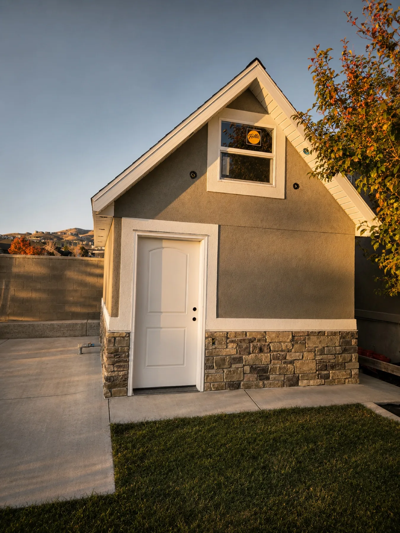Detached stucco outbuilding with stone wainscot at golden hour